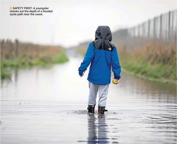  ?? ?? ■ SAFETY FIRST: A youngster checks out the depth of a flooded cycle path near the coast.