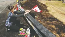  ?? TIM KROCHAK / REUTERS FILES ?? Care worker and first responder Alicia Cunningham adjusts a Canadian
flag at a makeshift memorial for slain RCMP Const. Heidi Stevenson.