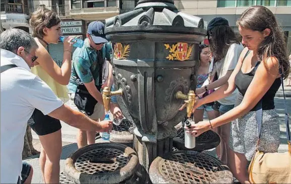  ?? GEMMA MIRALDA ?? Turistas acalorados rellenan botellines y cantimplor­as con agua de la fuente de Canaletes en la Rambla