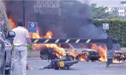  ?? - AFP ?? IN FLAMES: Two men stand next to burning cars at the scene of an explosion at a hotel complex in Nairobi on January 15, 2019.