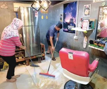  ?? — Bernama photo ?? Anis Syazwani Rashid, 26, and her husband conduct post-flood cleanup at their barbershop which they run from their house in Kampung Bukit Balai in Durian Tunggal, Melaka.