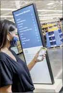  ?? Walmart / Mark Steele + FITCH photo via AP ?? A woman looks at her smartphone near a digital store directory inside the Walmart Supercente­r in Springdale, Ark., in July. Walmart is revamping the layout and signage of its stores to speed up shopping.