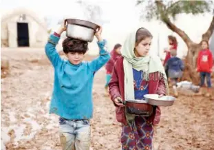  ?? Agence France-presse ?? NO END TO MISERY: A Syrian boy and girl carry pots of food while walking in the mud at a camp for the displaced near the village of Shamarin in the northern Aleppo province on Thursday.