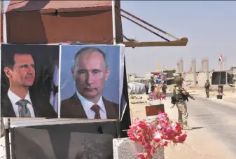  ?? George Ourfalian / AFP / Getty Images ?? Russian and Syrian troops stand guard near posters of Syrian President Bashar Assad and Russian President Vladimir Putin at a checkpoint on the eastern edge of Idlib province.