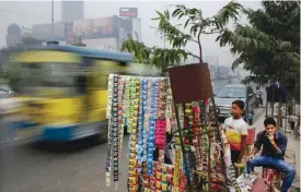  ??  ?? NEW DELHI: An Indian man smokes a cigarette sitting next to a roadside vendor selling tobacco products.