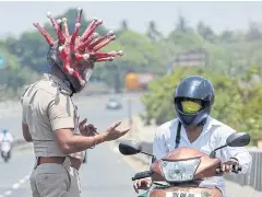  ?? REUTERS ?? A police officer with a helmet depicting the coronaviru­s requests a commuter to stay at home during a 21-day nationwide lockdown in India on Saturday.