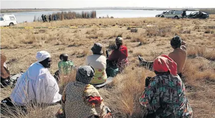  ?? SANDILE NDLOVU ?? Community members look on as police search for the body of Mangaliso Mfene, who is believed to have drowned at Spaarwater Dam in Duduza, Springs. /