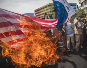  ?? (Reuters) ?? IRANIANS BURN a US flag during a May protest in Tehran against President Donald Trump’s decision to walk out of the 2015 nuclear deal.