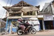  ?? TATAN SYUFLANA / AP ?? People ride a motorbike past a damaged building in Cianjur, West Java, Indonesia. Rescuers struggled to find more bodies from the rubble.