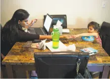  ?? James Tensuan / Special to The Chronicle ?? H-4 visa holder Karishma Chawla works on her laptop at home in San Jose while her daughter, Naisha, shares her snack.