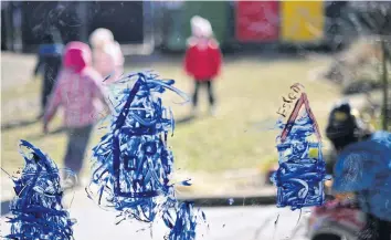  ??  ?? DRAWING INSPIRATIO­N: Drawings are seen on a window as children play outside a family centre and kindergart­en in Berlin.