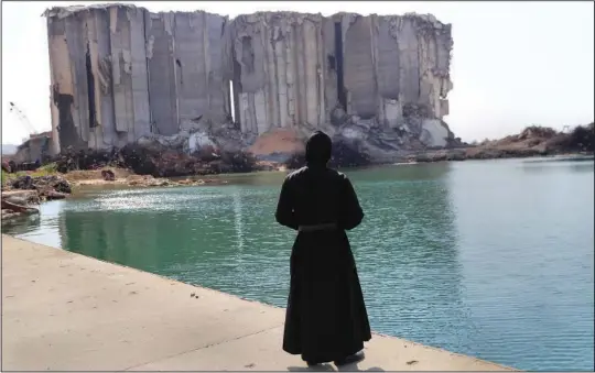  ?? (AP/Hussein Malla) ?? A priest looks toward towering grain silos Wednesday at the Beirut seaport in Lebanon. The silos were gutted in the massive explosion in August 2020.