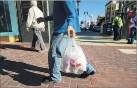  ?? Kimberly White Getty Images ?? A MAN carries a single-use plastic bag in San Francisco on Sept. 30, 2014, the same day Gov. Jerry Brown signed the nation’s first statewide ban on the bags.