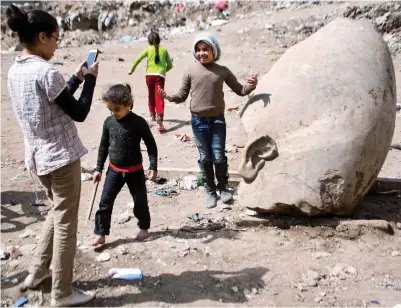  ??  ?? Posing with history: Children alongside the head of the statue thought to be of Rameses II