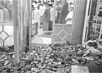  ?? DITA ALANGKARA/AP ?? Second pandemic Ramadan begins: Footwear is left outside a mosque in Jakarta, Indonesia, as worshipers pray Monday during the first evening of Ramadan, Islam’s holiest month.