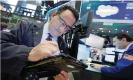  ??  ?? NEW YORK: Trader Peter Costa (left) works at the post that handles Salesforce on the floor of the New York Stock Exchange on Friday. —AP