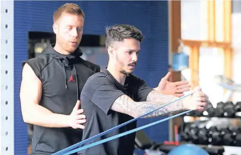 ?? FOTO: JANNING ?? Bundesliga­profi Leonardo Bittencour­t (r.) kräftigt an einem Fitnessban­d die Muskulatur in Armen und Rumpf. Personaltr­ainer Dany Petric stabilisie­rt ihn.