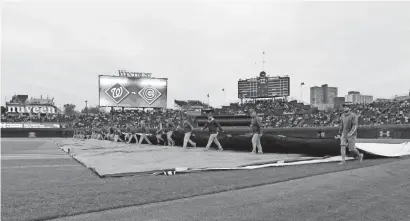  ?? DENNIS WIERZBICKI/USA TODAY SPORTS ?? The Cubs grounds crew roll out the tarp before Game 4 of the National League Division Series against the Nationals Tuesday at Wrigley Field in Chicago. The game was postponed and will be played on Wednesday.