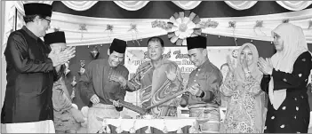  ??  ?? Ting (centre) witnesses a ‘lemang’ (glutinous rice cookd in bamboo) being opened, which marks the start of the Hari Raya Aidilfitri get-together at SM Sains Miri. The assemblyma­n is flanked by Dzul Badzil on his right and Nazri.