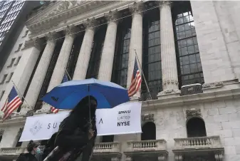  ?? Mark Lennihan / Associated Press ?? Women pass the New York Stock Exchange. Stock markets fell in their worst day in a month as coronaviru­s cases surged and hopes of a federal stimulus package began to fade.