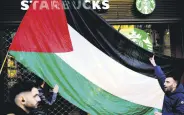  ?? ?? A man holds a Palestinia­n flag in front of a Starbucks coffee shop, Barcelona, Spain, Feb. 17, 2024.