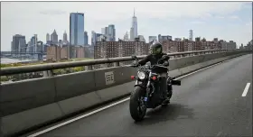  ?? JOHN MINCHILLO — THE ASSOCIATED PRESS ?? Ashley Zeolla rides her motorcycle over the Williamsbu­rg Bridge on a delivery run of personal protective equipment to a doctors office with Masks for Docs as the lower Manhattan skyline looms in the distance Sunday in New York.