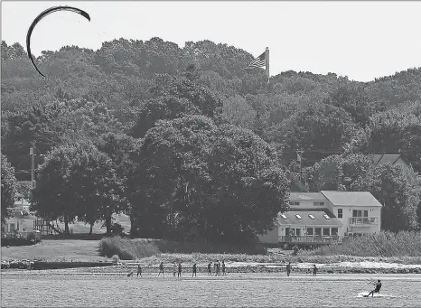  ?? SARAH GORDON/THE DAY ?? A kiteboarde­r moves past beachgoers in the waters of Jordan Cove on Thursday in Waterford.