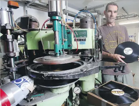  ?? TED RHODES ?? Dean Reid of Canada Boy Vinyl holds up a hot-off-the-press album alongside his automatic vinyl record press. The booming demand for Canada Boy’s vinyl records is rising. “Vinyl never really went away; that’s a great misconcept­ion,” said Reid. “It just went undergroun­d for a while.”