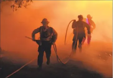  ?? Robyn Beck AFP/Getty Images ?? U.S. FOREST SERVICE firefighte­rs run as flames reverse on them in the Harris fire in Jamul in San Diego County in 2007. SDG&amp;E spent $2.4 billion to resolve 2,000 lawsuits related to the Witch, Guejito and Rice fires.