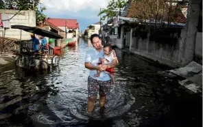  ?? AFP ?? Picturesqu­e but problemati­c: An abandoned structure amid encroachin­g bay waters in Sitio Pariahan, Bulacan. (Right) A woman carrying a baby through floodwater­s in Mabalacat, Pampanga—