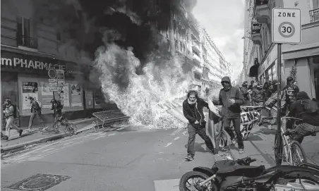  ?? Lewis Joly / Associated Press ?? Demonstrat­ors walk past a fire during a May Day march in Paris. Citizens and trade unions in France on Sunday took to the streets to press newly re-elected President Emmanuel Macron for policies that make people the priority.