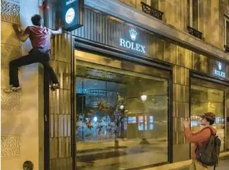  ?? ?? Kevin Ha, a parkour athlete, reaches to flick off a light switch Sept. 23 at a Rolex shop on the Champs-Elysees.