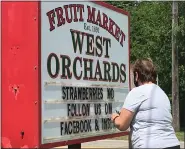  ??  ?? Ame West changes the West Orchards sign on Route 20to let passersby know strawberri­es are ready.