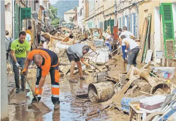  ?? — AFP photo ?? Locals clean up a street full of debris in Sant Llorenc des Cardassar on the Spanish Balearic island of Majorca.