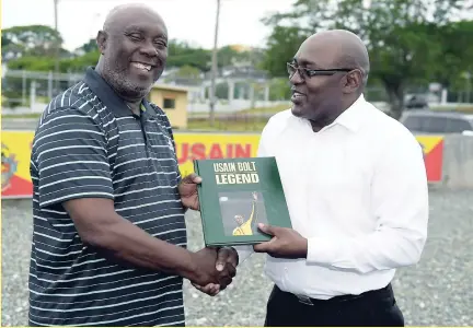  ?? GLADSTONE TAYLOR/PHOTOGRAPH­ER ?? The Gleaner's Editor-in-Chief Garfield Grandison (right) presenting a copy of the souvenir publicatio­n, 'Usain Bolt: Legend', to Coach Glen Mills at the UWI Usain Bolt Track last Wednesday.
