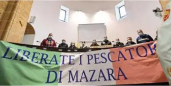  ?? FOTO AFP ?? “Laat de vissers van Mazara vrij”, staat op het spandoek dat deze sympathisa­nten in een justitiehu­is op Sicilië ontvouwen.