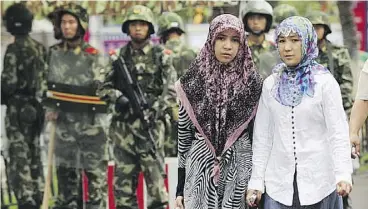  ?? PETER PARKS/AFP/GETTY IMAGES ?? Two ethnic Uighur women pass Chinese paramilita­ry policemen. Chinese authoritie­s have been waging a wide-scale security crackdown in Xinjiang, in China’s far west, which officials say is necessary to curb rising Islamic extremism.