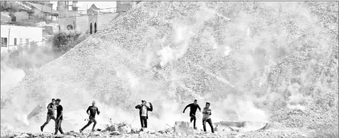  ?? — AFP photos ?? Palestinia­n protesters run for cover from an incoming teargas volley during clashes with Israeli forces following a demonstrat­ion near the Israeli settlement of Beit El in the Israeli occupied West Bank.