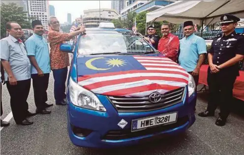  ?? PIC BY NUR ADIBAH AHMAD IZAM ?? Federal Territorie­s Minister Khalid Abdul Samad (third from left) attaching a Jalur Gemilang to a taxi at the Dang Wangi police station in Kuala Lumpur yesterday. With him are City police chief Datuk Seri Mazlan Lazim (fourth from right) and Selangor Indian Muslim Taxi Drivers Welfare Associatio­n adviser Datuk Jawahar Ali (third from right).