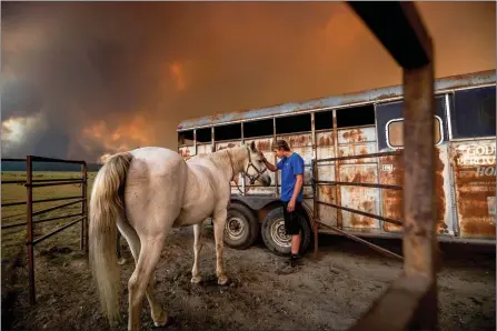  ?? The Associated Press ?? Hunter McKee pets Rosy after helping evacuate the horse to the edge of Lake Almanor as the Dixie Fire approaches Chester, Calif, on Tuesday. Officials issued evacuation orders for the town earlier in the day as dry and windy conditions led to increased fire activity.
