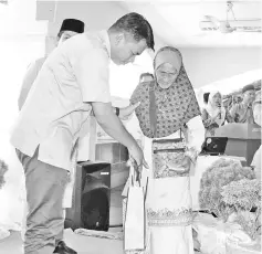  ??  ?? Azis (left) helping Embai bt Peraman, one of the 10 single mothers, down the stage after the latter received gifts and donation at the event yesterday.