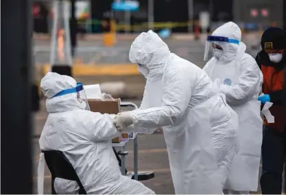  ?? PAT NABONG/SUN-TIMES ?? Medical personnel help each other suit up at a federal COVID-19 drive-thru testing site in Northlake in March 2020. The state had just gone into lockdown.