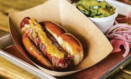  ?? J.C. Reid / Contributo­r ?? Blood Bros. BBQ offers a bacon-wrapped hotlink-style dog call the Ripper.