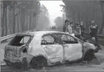  ?? ARMANDO FRANCA, THE ASSOCIATED PRESS ?? Police stand by a burnt-out car in Portugal on Sunday. The prime minister called fire deaths “a tragedy beyond any in our memory.”