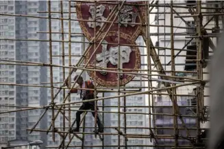  ?? AFP ?? This picture taken in Hong Kong on March 9, 2023 shows a sca older constructi­ng bamboo sca olding around a neon sign. The world’s most skyscraper-laden metropolis is also one of the last remaining major cities to use bamboo sca olding for modern constructi­on and building repair.