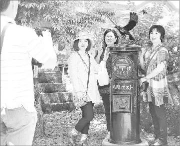  ?? — Japan News-Yomiuri photo ?? Women display amulets in front of a Yatagarasu statue at Kumano Hongu Taisha shrine in Tanabe, Wakayama Prefecture.