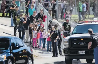  ?? GINA FERAZZI, TNS ?? San Bernardino police officers escort children to waiting school buses after Monday’s shooting at North Park School in San Bernardino, California.