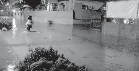  ?? IVY C. TEJANO ?? FLOODED. A street in NHA Bangkal is already knee-high by midnight yesterday, prompting residents to venture out to safer grounds. NHA Bangkal is known to be flood-prone as the Pangi River runs around it.