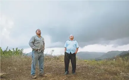  ?? Photos by Dennis M. Rivera Pichardo, The Associated Press ?? Retired resident Ramon Serrano, right, stands outside his home Friday with a lineman from the Puerto Rico Power Authority as they watch a man restore power, which was cut off by Hurricane Irma and Maria in Adjuntas, Puerto Rico. For the first time in 10 months, Serrano watched the news on a recent weeknight and went to bed at midnight with his wife. “It's the latest we've been up,” said the 77-year-old.