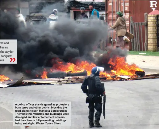  ?? Photo: Zolani Sinxo ?? A police officer stands guard as protesters burn tyres and other debris, blocking the road along Nelson Mandela Boulevard in Thembaleth­u. Vehicles and buildings were damaged and law enforcemen­t officers had their hands full preventing buildings being...